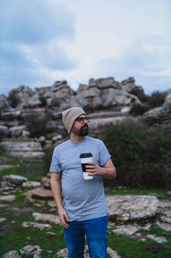 A beautiful shot of an adult Caucasian man holding his coffee while standing in El Torcal de Antequera during daytime, Malaga, Spain