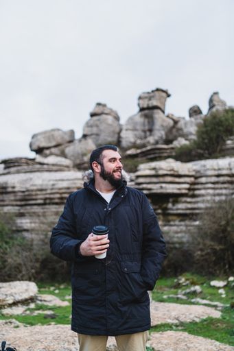 A beautiful shot of a smiling adult Caucasian man holding his coffee and standing in El Torcal de Antequera during daytime, Malaga, Spain