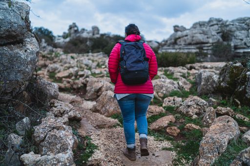 A back shot of an adult Caucasian woman wearing a backpack and walking in El Torcal de Antequera during daytime, Malaga, Spain