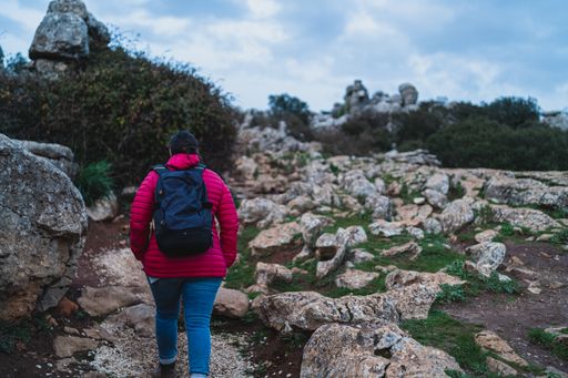 A back shot of an adult Caucasian woman wearing a backpack and walking in El Torcal de Antequera during daytime, Malaga, Spain