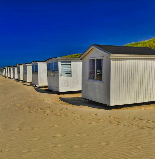A vertical shot of a row of white wooden beach huts against blue sky