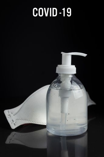A vertical shot of a face mask and hand sanitizer on a black background - concept of important preventive measures against the COVID19 virus