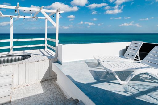 a sunny deck with 2 loungers next to the sea on a top story of a building