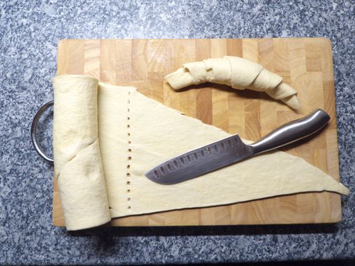 A top view of a dough and a raw croissant on a wooden cutting board