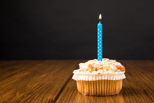 A muffin with a burning candle on a wooden table on a black background with copy space