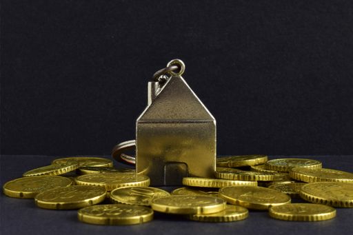 a close up shot of small metal house and scattered coins on the black background.
