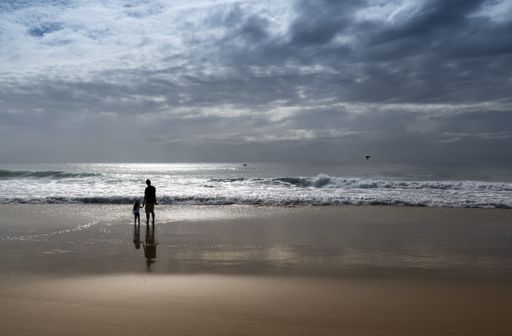A silhouette views of an unrecognizable father and daughter in the shallows on the Sunshine Coast of Old, Australia
