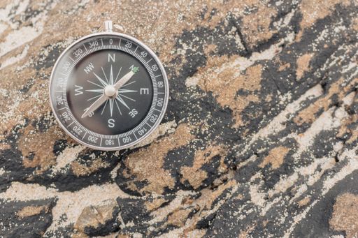 A compass on a beautifully colored rock with beach sand on it