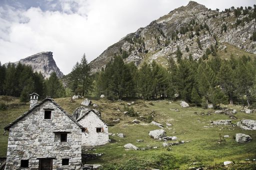 Two old buildings surrounded by rocks covered in greenery under a cloudy sky in the countryside