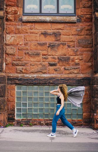 A side shot of a  caucasian young girl walking with an old brick building on the background