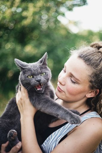 A vertical shot of a beautiful young woman holding her angry looking cat in summer or spring