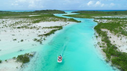 An aerial view of people sailing down a river in a white tiny boat at Exumas, Bahamas