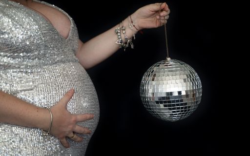 A horizontal shot of a pregnant female holding a silver disco ball on a black background