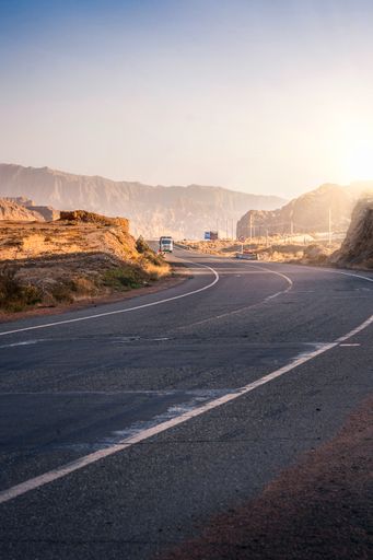 A vertical shot of an empty highway amid cliffs under the clear sky