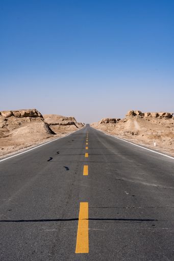 A vertical shot of an empty highway amid cliffs under the clear sky