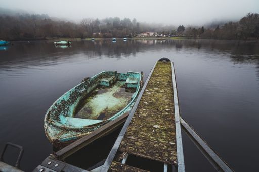 A high angle shot of a dirty old boat parked near the pier in the lake