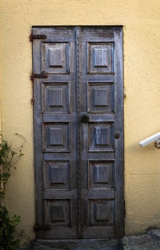 A vertical shot of an old wooden door of a building with light yellow walls