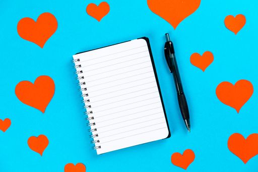 A top view of a notebook with pen on a blue background with red hearts