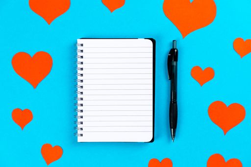 A top view of a paper with pen on a blue background with red hearts