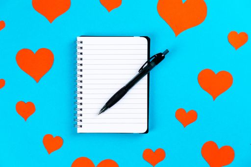 A top view of paper with pen on a blue background with red hearts