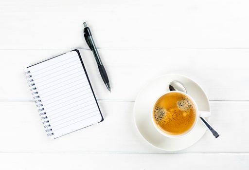 A top view of a coffee cup with paper and pen on a white wooden background