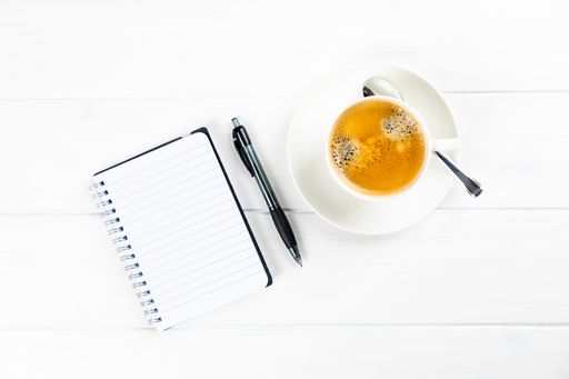 A top view of a coffee cup with paper and pen on a white wooden background