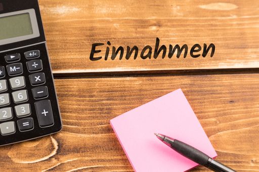 A top view of a wooden business desk with paper, pen and calculator with a German text "Einnahmen"-meaning revenue