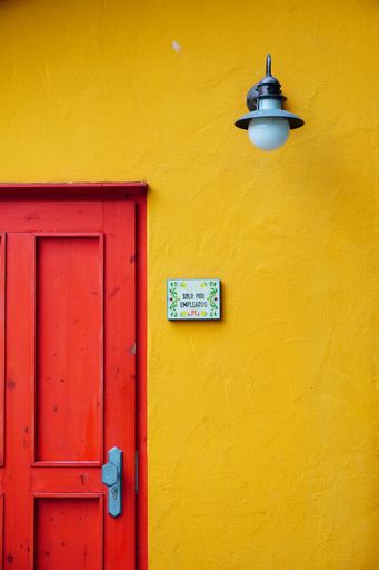 A vertical shot of a red wooden door with a lamp on a yellow wall