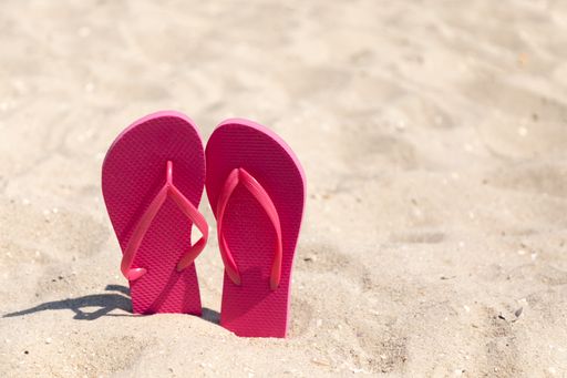 A closeup of pink flip flops on a sandy beach
