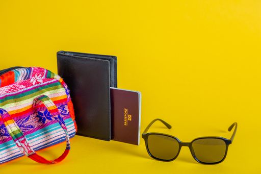 A closeup of travel document, sunglasses, and purse isolated on a yellow background- travel concept
