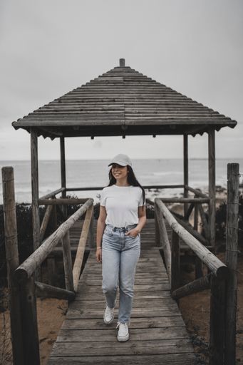 A beautiful shot of a Caucasian girl walking on a wooden pier on the beach with the sea and a gray sky in the background
