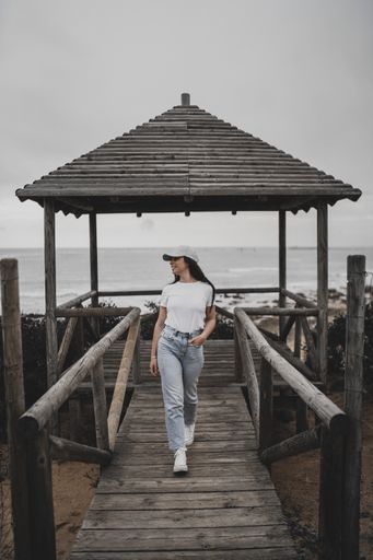 A beautiful shot of a Caucasian girl walking on a wooden pier during daytime with seascape and cloudy sky in background