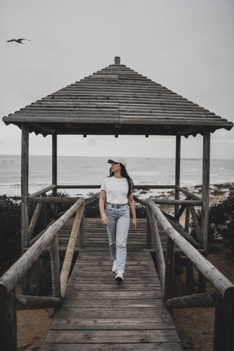 A vertical shot of a young woman walking along a wooden pier against the background of the ocean