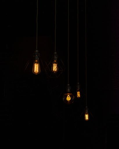 A vertical shot of illuminated hanging filament bulbs in the dark