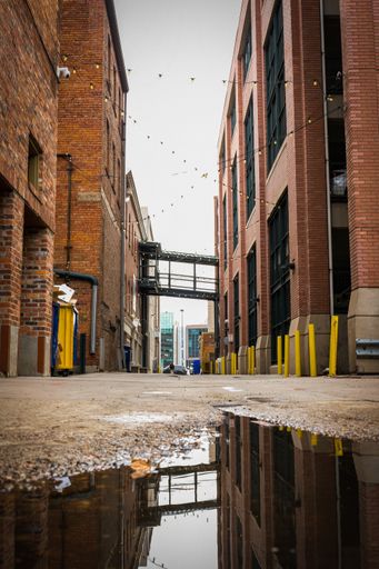 A closeup shot of a small puddle in a narrow ally in Denver downtown reflected the ally bridge and buildings around it during daytime