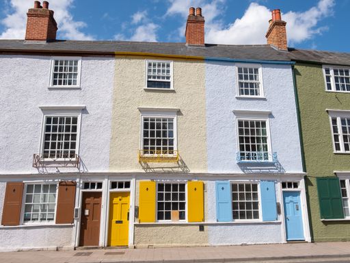 Three stucco brick houses are attached with chimnies and brown, yellow, and blue colored doors along a street in Oxford on a bright sunny day.