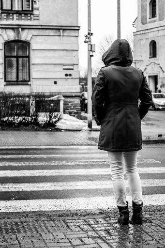 A vertical shot of a female with a coat standing on the street on a rainy day shot in grayscale