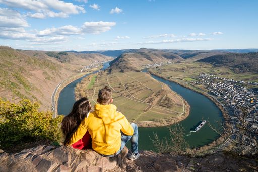 A high angle shot of a young couple sitting at the gorge edge enjoying the fascinating view of the lake and mountains
