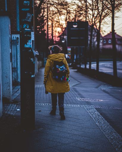 A back shot of a female with a yellow long coat walking on the side street in Eberswalde, Germany at sunset time