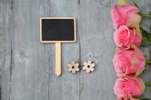 A top view of pink rose flowers and a chalkboard with space for text on a wooden surface