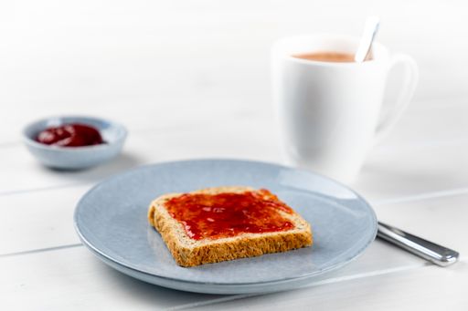 A closeup shot of toast with strawberry jam on a blue plate and a cup of cacao on a white wooden background