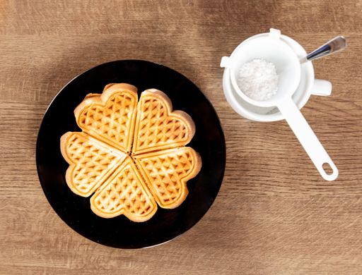 fresh waffle on a black plate with powdered sugar in a white strainer on a wooden background
