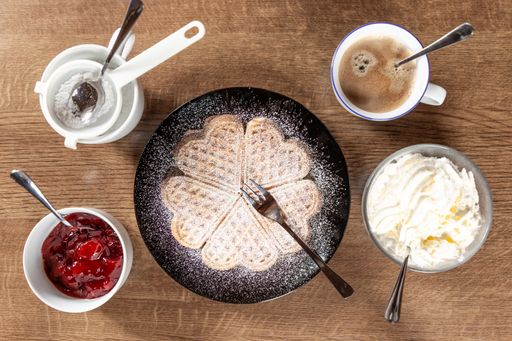 fresh waffle on a black plate with jelly, ice cream, powdered sugar in white bowls and cup of coffee on a wooden background
