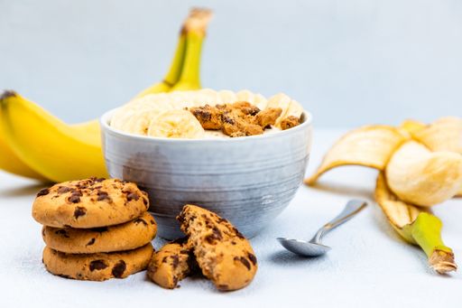 A closeup shot of cream dessert with banana fruit in a bowl and cockies on blue background