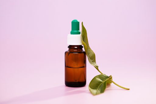 A closeup of medicinal leaf extracts in a medicine bottle over a pink background
