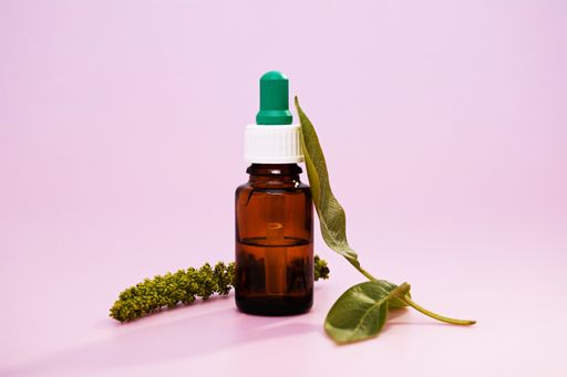 A closeup of medicinal leaf extracts in a medicine bottle over a pink background