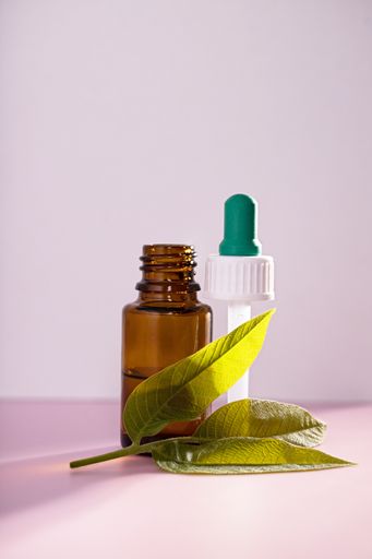 A closeup of medicinal leaf extracts in a medicine bottle over a pink background