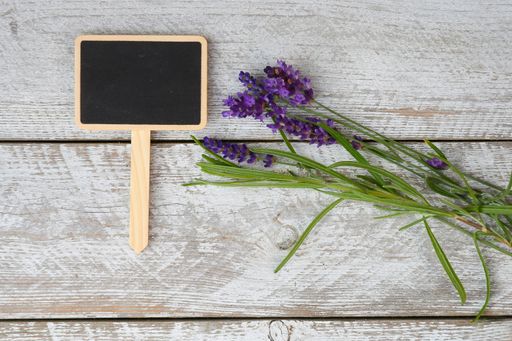 A top view of a chalkboard with space for text next to lavender flowers on a wooden surface