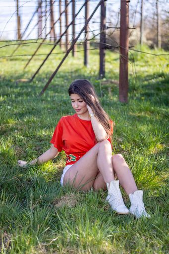 A beautiful woman in a red shirt sitting on the green grass on a sunny day.Beautiful nature, comfort, travel, village.