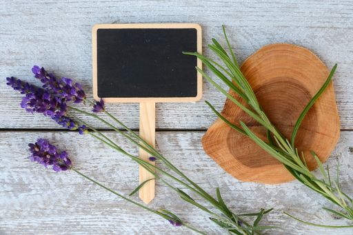 A top view of a chalkboard with space for text next to lavender flowers on a wooden surface